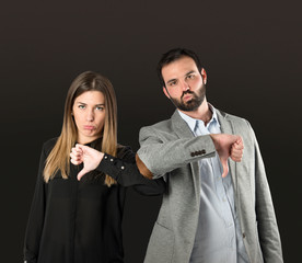 Couple with their thumbs down over black background