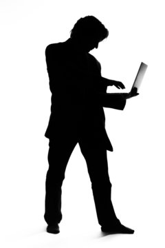 Silhouette of a man in suit typing on a laptop