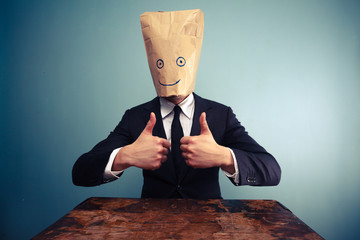 Businessman with bag over head giving thumbs up - obrazy, fototapety, plakaty