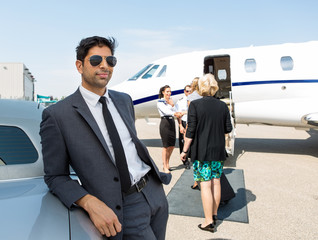 Businessman Leaning On Car At Airport Terminal
