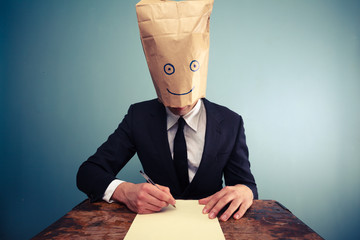 Businessman with bag over head writing at desk