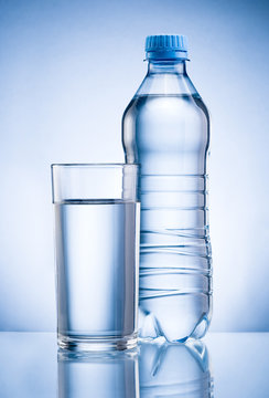 Plastic bottle and glass of drinking water isolated on blue back
