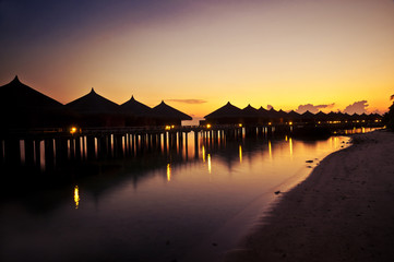 Obraz premium Tropical huts along a beach at sunset