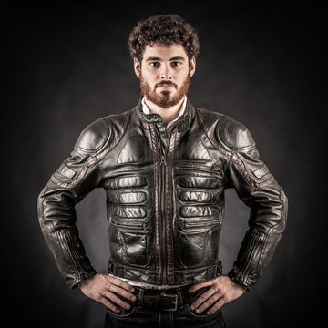 Portrait of confident young man wearing leather jacket against b