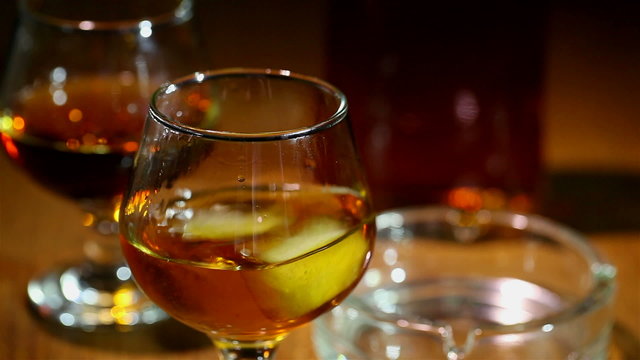 Ice falls in a glass with cognac, whisky close up