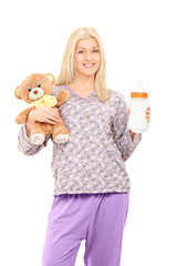 Young woman in pajamas holding teddy bear and baby bottle