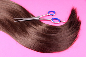 Long brown hair with scissors on pink background