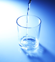 Pour water from  pitcher into  glass, on dark blue background