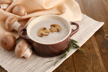 Mushroom soup in pot, on wooden background