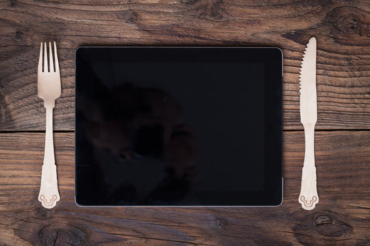 empty tablet computer fon a table with knife an fork .