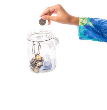 A little girl hands putting coin in a money jar.