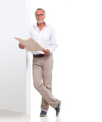 Mature man with newspaper leaning against a wall