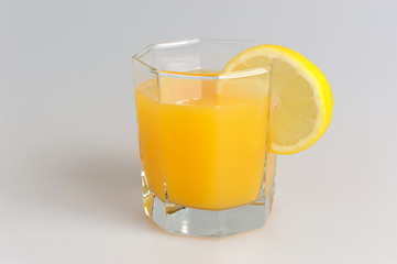 Glass with a slice of lemon filled with citrus juice on grey