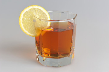 Glass with a slice of lemon filled with lemon tea on grey