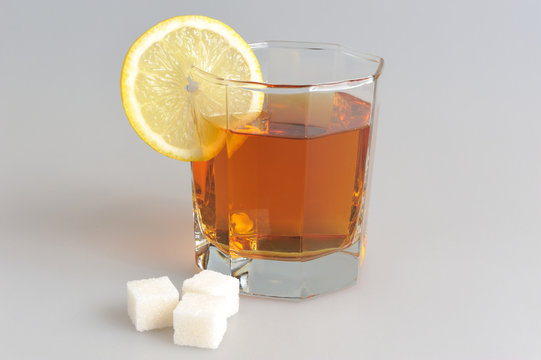Glass with a slice of lemon filled with lemon tea and refined su