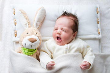 Cute yawning baby girl in а crib with a toy rabbit