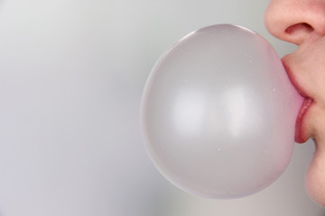 Person doing bubble with chewing gum on bright background