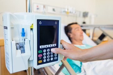 Nurse Operating IV Machine While Patient Lying On Bed
