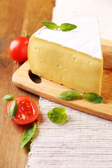 Tasty Camembert cheese with tomatoes and basil, on wooden table