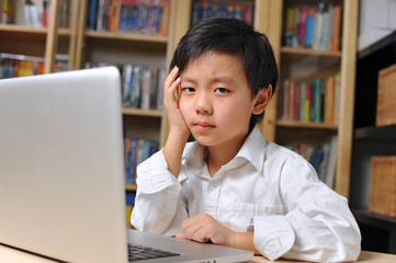 Unhappy Chinese school boy in front of laptop computer