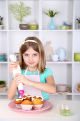 Little girl decorating cupcakes in kitchen at home