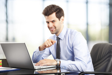 Happy young businessman using laptop in his office