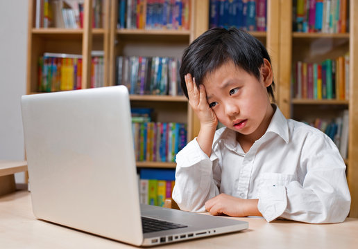 Frustrated Asian school boy in white shirt looking at computer
