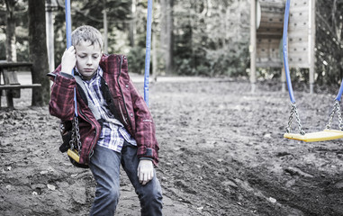 Sad or depressed boy sitting in playground swing