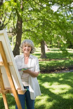 Smiling mature woman painting on canvas in park