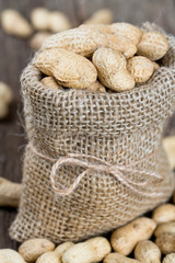 peanuts in a miniature burlap bag on wooden surface
