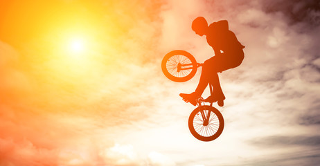 Mann, der einen Sprung mit einem bmx-Fahrrad gegen Sonnenscheinhimmel tut.