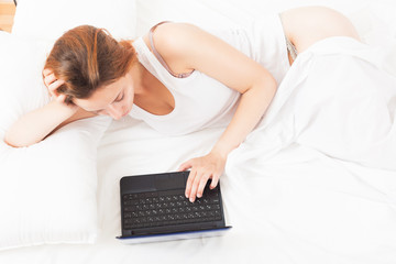 Red-haired woman awake with laptop  on her bed