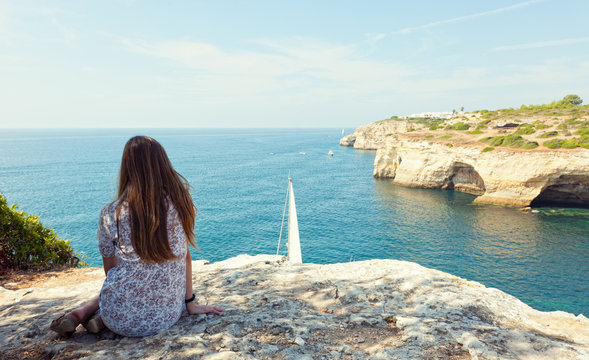 girl sits on the rock and looks at yachts at the ocean
