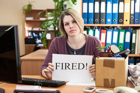 Sad woman with collected things and paper with word "Fired"