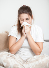 Young brunette woman sitting on bed and sneezing