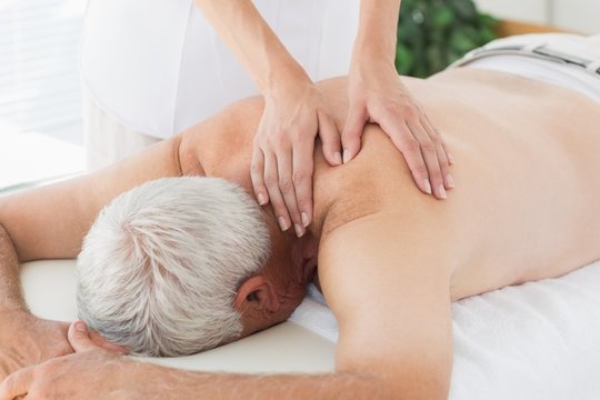 Therapist massaging back of senior man