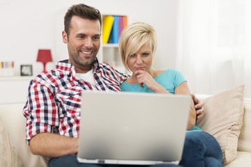 Young couple sitting on sofa and using laptop at home .