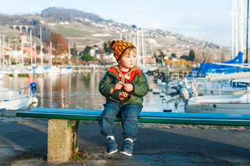 Outdoor portrait of a cute toddler boy sitting on a bench