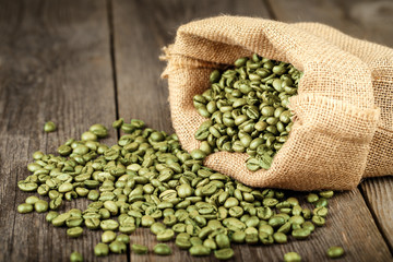 Green coffee beans in bag made from burlap on wooden surface