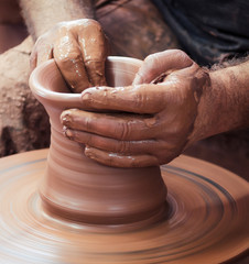 Potter hands making in clay on pottery wheel.