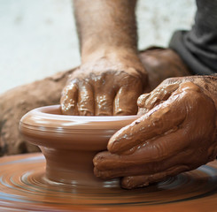 Potter hands making in clay on pottery wheel.