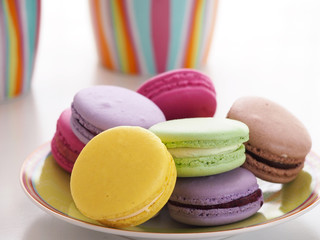 Colorful macaroons on plate and cups in background