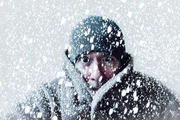Freezing cold man shivering in a snowstorm with hat and coat and snowflakes blowing all around him.