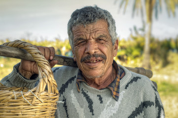 Senior farmer holding a fork and a straw basket in the fields