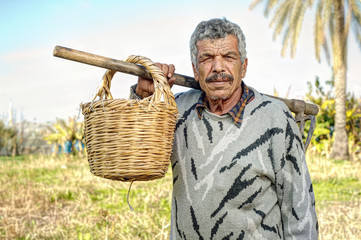 Senior farmer holding a fork and a straw basket in the fields