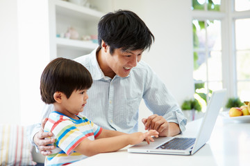 Asian Father Helping Son To Use Laptop At Home