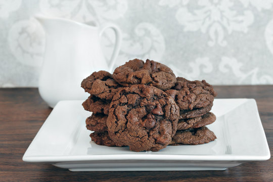 A stack of chocolate, chocolate chip cookies on a white plate.
