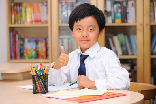 Asian schoolboy sitting at a desk and showing thumb up