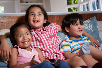 Three Asian Children Sitting On Sofa Watching TV Together