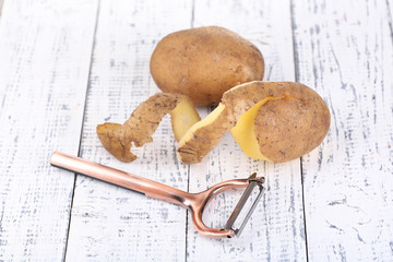 Peeler and fresh potato on color wooden background